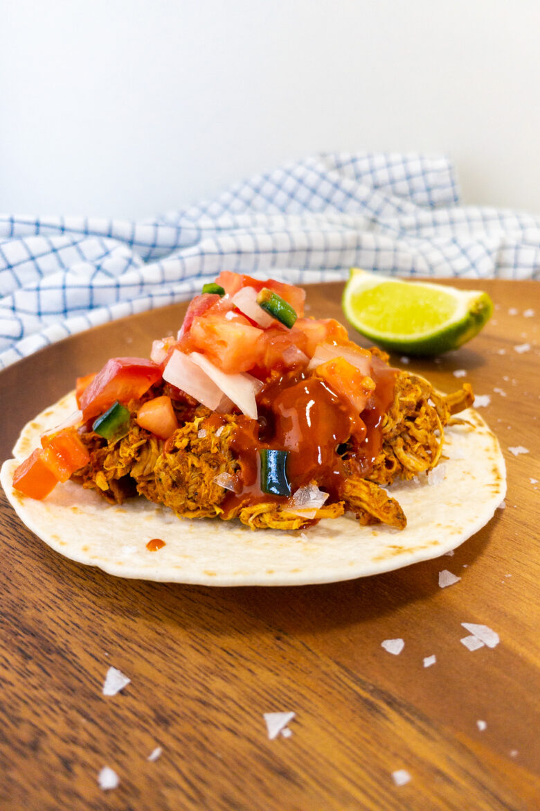 Mexicaans recept voor taco's met pollo pibil op een houten ondergrond. Daarbij limoenen en zout