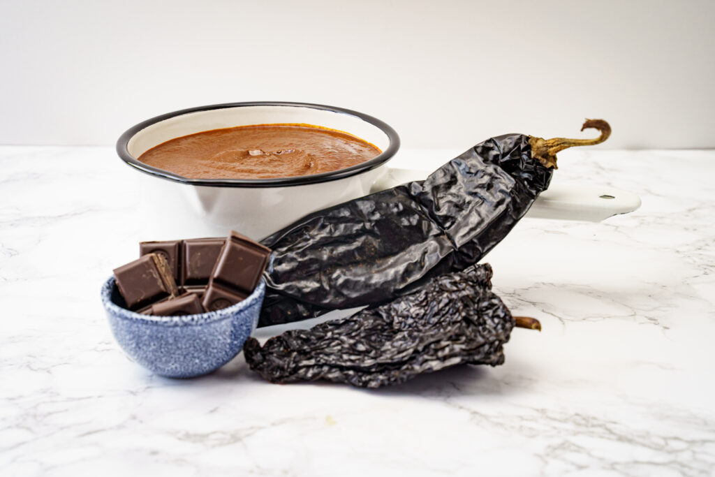 Mole de poblano in een pan met daarvoor chocolade en pepers