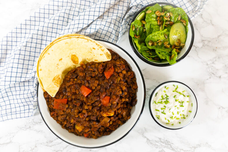 Mexicaans recept voor chili sin carne. Je ziet een bord met daarin de chili en tortilla's. Daarnaast staat een bakje salade én een bakje met de saus.